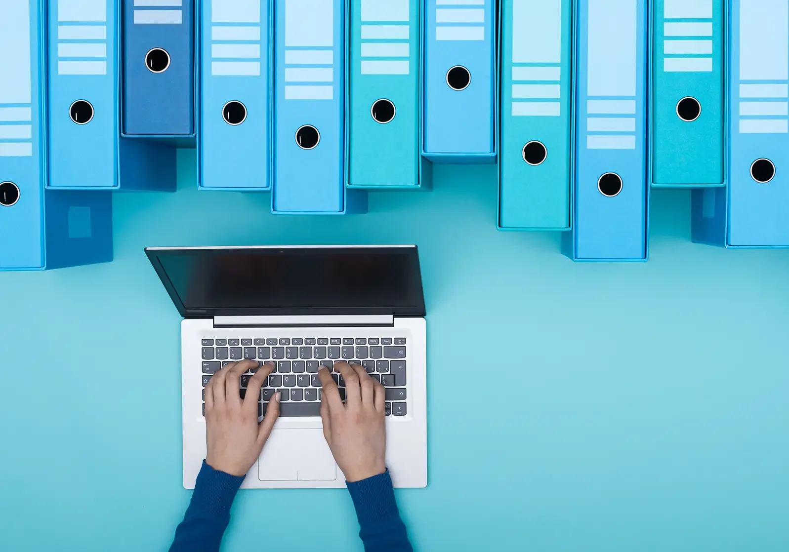 Photo of a person typing on a laptop next to archive boxes.