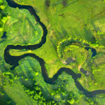 Aerial photo of a green field with a river curving through it.